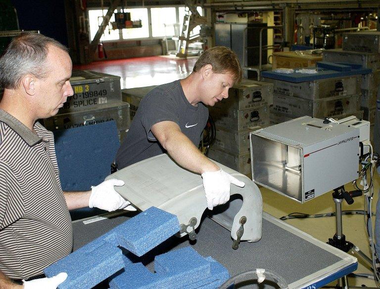 KENNEDY SPACE CENTER, FLA. - In the Orbiter Processing Facility, United Space Alliance workers Dan Kenna and Jim Landy prepare to examine a Reinforced Carbon Carbon panel using flash thermography. Attached to the leading edge of the wing of the orbiters, the gray carbon composite RCC panels have sufficient strength to withstand the aerodynamic forces experienced during launch and reentry, which can reach as high as 800 pounds per square foot. The operating range of RCC is from minus 250º F to about 3,000º F, the temperature produced by friction with the atmosphere during reentry.