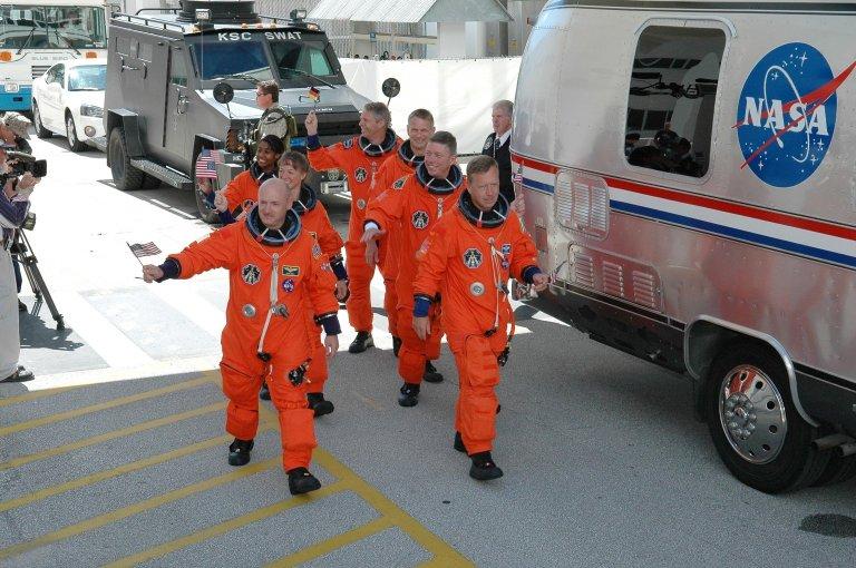 KENNEDY SPACE CENTER, FLA. - Waving flags for the Fourth of July, the STS-121 crew heads for the Astrovan and the ride to Launch Pad 39B for a third launch attempt. Leading the way are Pilot Mark Kelly (left) and Commander Steven Lindsey (right). Behind them are, left and right, Mission Specialists (second row) Lisa Nowak and Michael Fossum; (third row) Stephanie Wilson and Piers Sellers; and (at the rear) Thomas Reiter, who represents the European Space Agency. The July 2 launch attempt was scrubbed due to the presence of showers and thunderstorms within the surrounding area of the launch site. The launch of Space Shuttle Discovery on mission STS-121 is the 115th shuttle flight and the 18th U.S. flight to the International Space Station. During the 12-day mission, the STS-121 crew will test new equipment and procedures to improve shuttle safety, as well as deliver supplies and make repairs to the International Space Station. Photo credit: NASA/Kim Shiflett